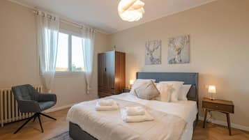 Ein Schlafzimmer mit Bett, Nachttischen, einem Sessel, einem Kleiderschrank und Bildern an der Wand.