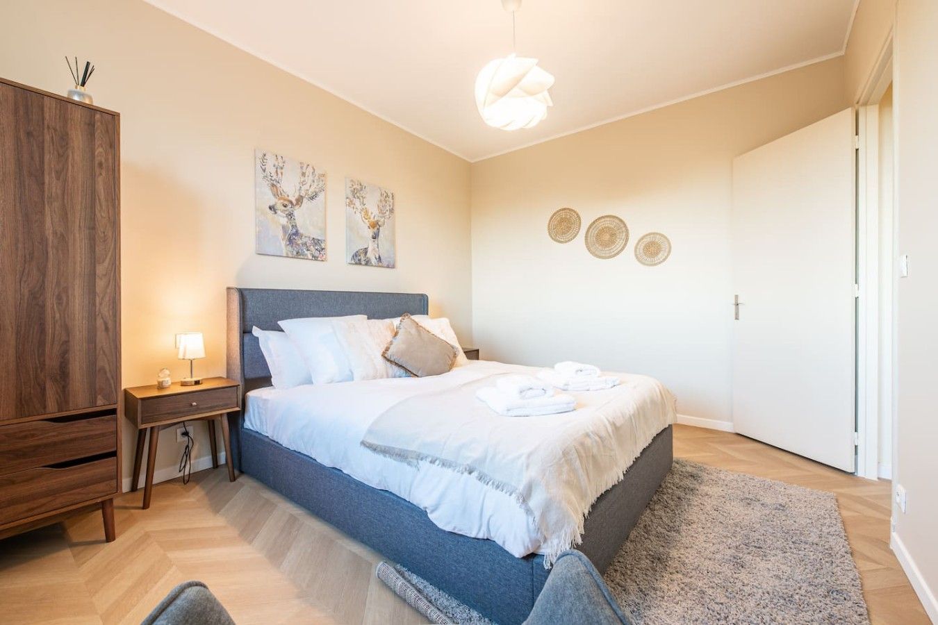 Ein Schlafzimmer mit einem Bett, Nachttischen, einem Kleiderschrank, Bildern an der Wand und einer Tür.