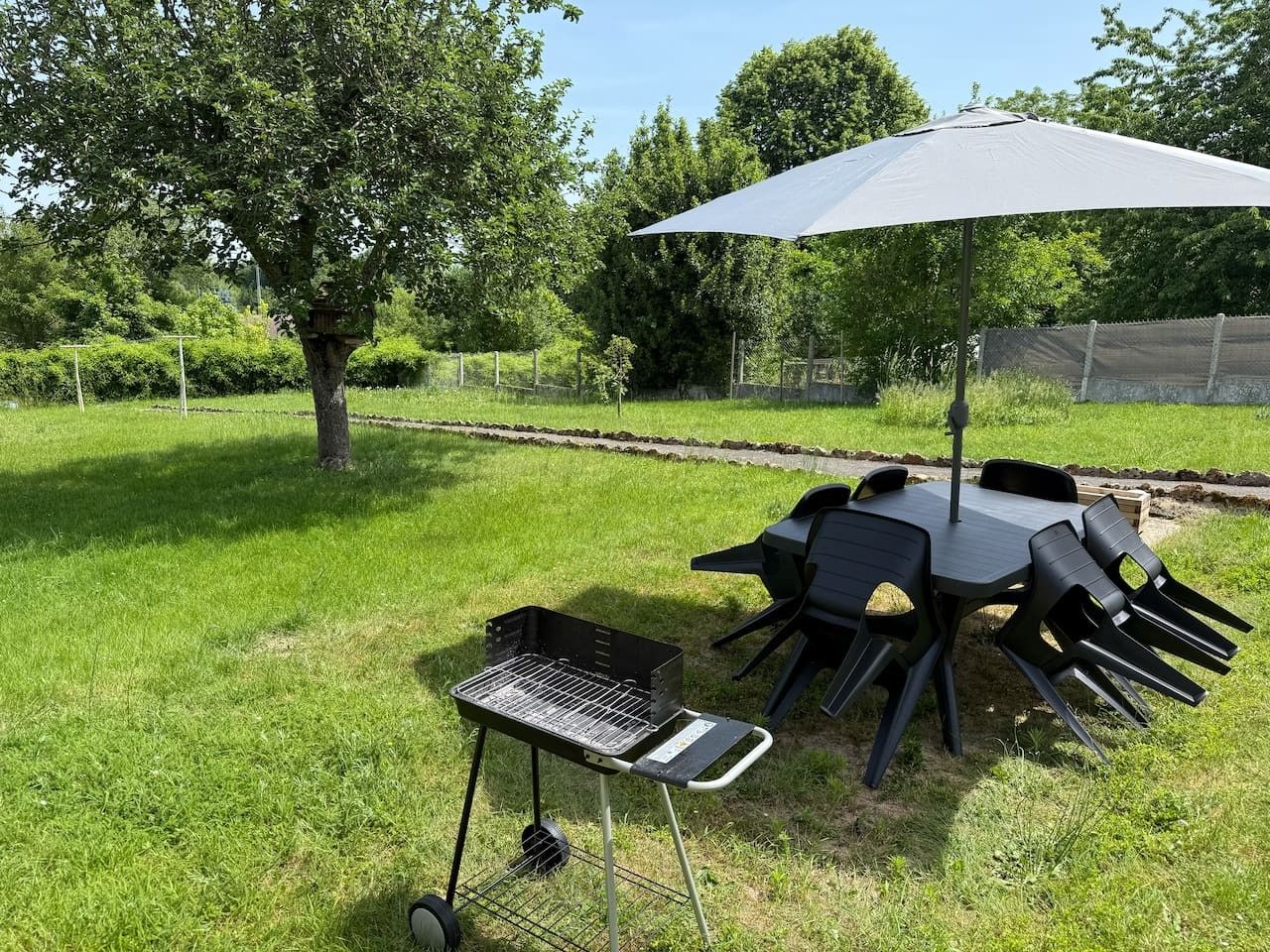 Een terras buiten met een barbecue, stoelen en een tafel onder een overkapping.