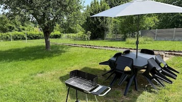 Een terras buiten met een barbecue, stoelen en een tafel onder een overkapping.