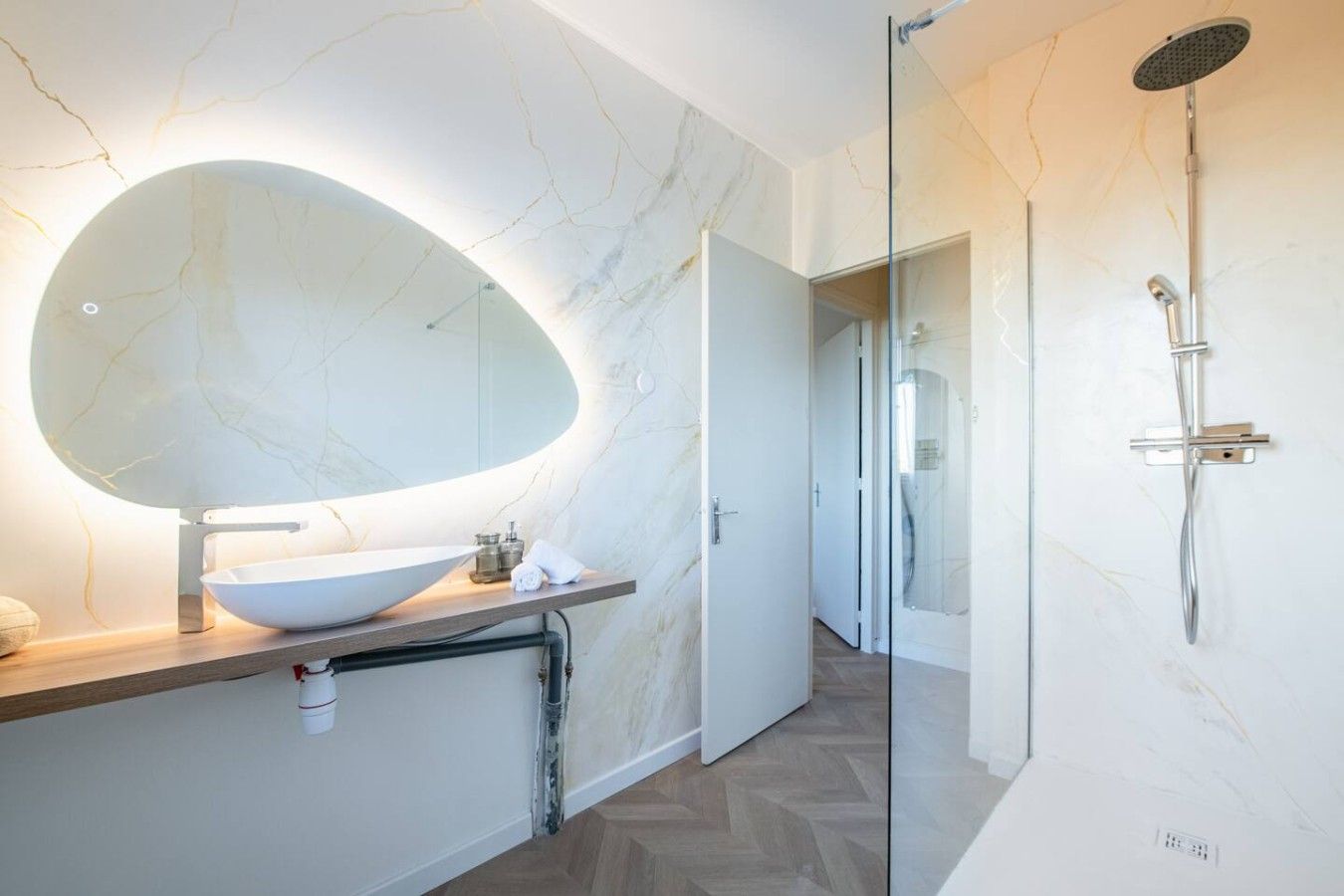 A modern bathroom with a large oval mirror, a vessel sink, and a glass-enclosed shower.