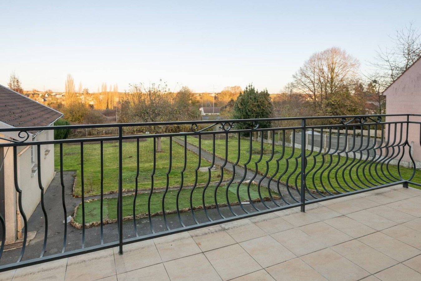 Een balkon met een metalen hekwerk, een geplaveid terras en uitzicht op een gazon met een pad.