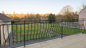 Een balkon met een metalen hekwerk, een geplaveid terras en uitzicht op een gazon met een pad.