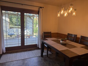 A dining area with a table set for four, a sliding glass door leading to an outdoor patio, and a hanging light fixture. - Your Home Base for OSU Game Days & Stillwater Stays (Stillwater)