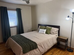 A bedroom with a bed, a bedside table, a floor lamp, and a window with curtains. - Your Home Base for OSU Game Days & Stillwater Stays (Stillwater)
