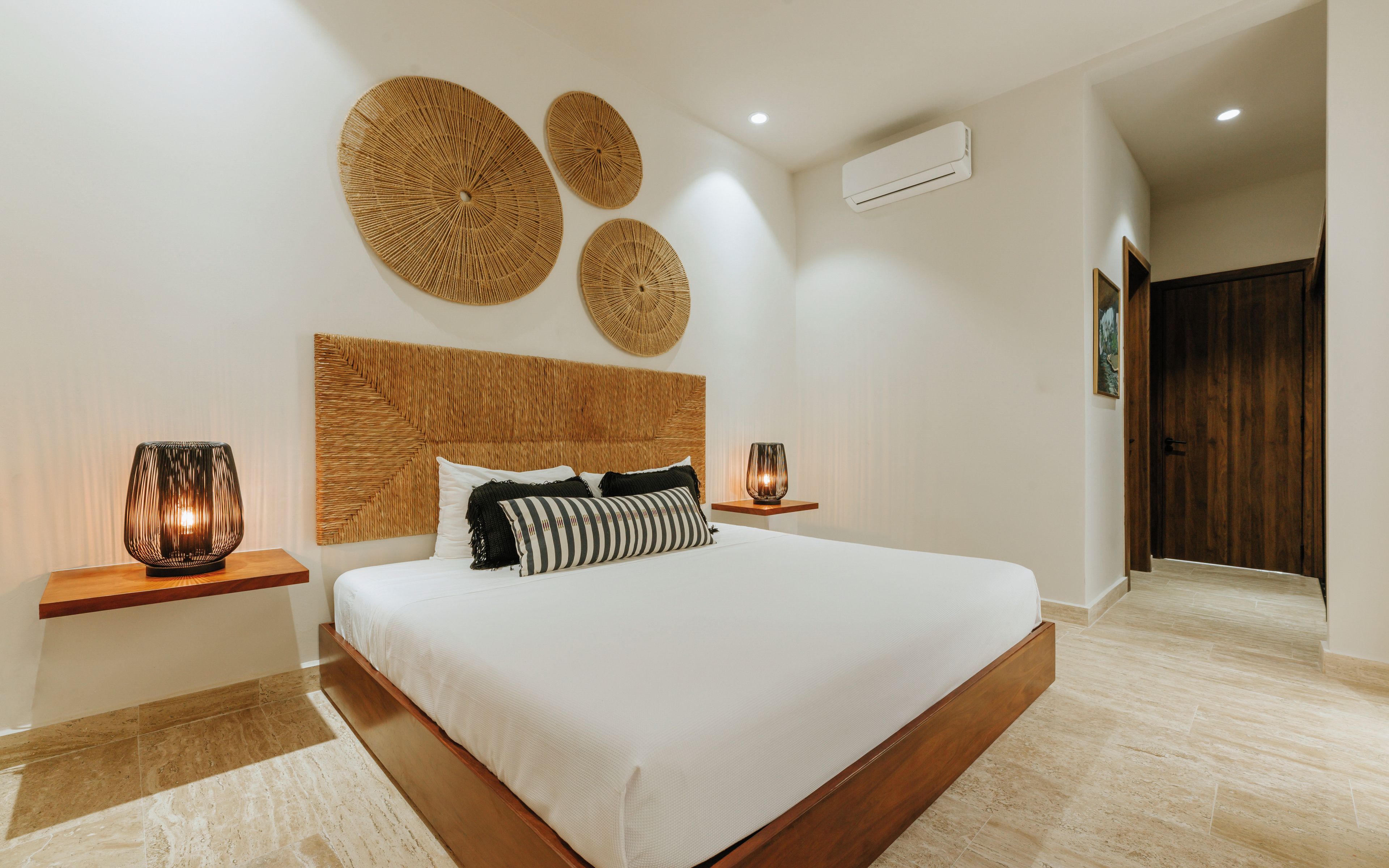 Quarto moderno com cama grande, duas mesas de cabeceira, cabeceira de madeira e arte decorativa na parede.