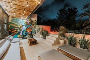 Un espacio al aire libre con un mural, escalones que conducen a una terraza y plantas en macetas.