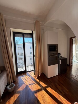 Eine moderne Küche mit eingebautem Backofen und Mikrowelle, einem kleinen Kühlschrank und einem Fenster mit Blick auf einen Balkon.
