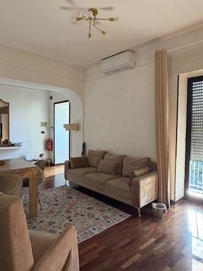Ein Wohnzimmer mit beiger Couch, einem Holzesstisch, einem gemusterten Teppich und einem Deckenventilator.