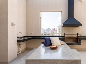 A modern kitchen with a large window, a built-in grill, and a minimalist design. - Edificio Parque Vivo by Domus Travels (Santiago)