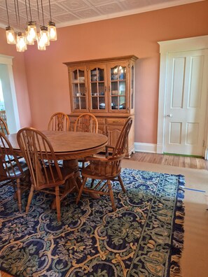 Comedor con una mesa redonda, sillas de madera, un tapete estampado y un aparador de madera con puertas de cristal.
