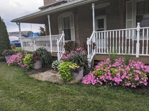 Una casa residencial con porche cubierto, plantas en macetas y césped.