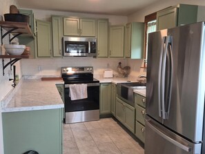 Una cocina con gabinetes verdes, un refrigerador de acero inoxidable, un microondas, un horno y un lavamanos.