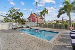 A swimming pool with lounge chairs, a fenced area, and a red building in the background. - 🐢The Turtle Nest | Private Heated Pool | Newly Built Home (Fort Myers beach)