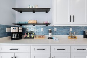 A modern kitchen with white cabinets, a coffee maker, tea bags, and a paper towel dispenser. - 🐢The Turtle Nest | Private Heated Pool | Newly Built Home (Fort Myers beach)