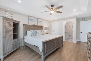 Ein Schlafzimmer mit einem Bett, einem Kleiderschrank, einem Deckenventilator und einem durchgegangenen Tür sichtbar liegenden Badezimmer.