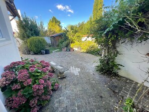 A paved courtyard with a stone bench, surrounded by lush greenery and a variety of plants. - A bright and elegant home (Chartres)