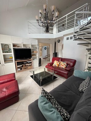 A modern living room with a flat-screen TV, a glass coffee table, red and black sofas, a red leather chair, and a staircase leading to an upper level. - A bright and elegant home (Chartres)