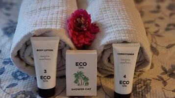 Trois serviettes roulées ornées d’un motif floral, une fleur rose et deux tubes de lotion corporelle et d’après-shampoing.