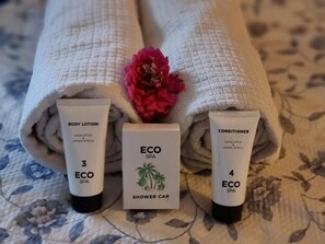 Three rolled towels with a floral pattern, a pink flower, and two tubes of body lotion and conditioner.