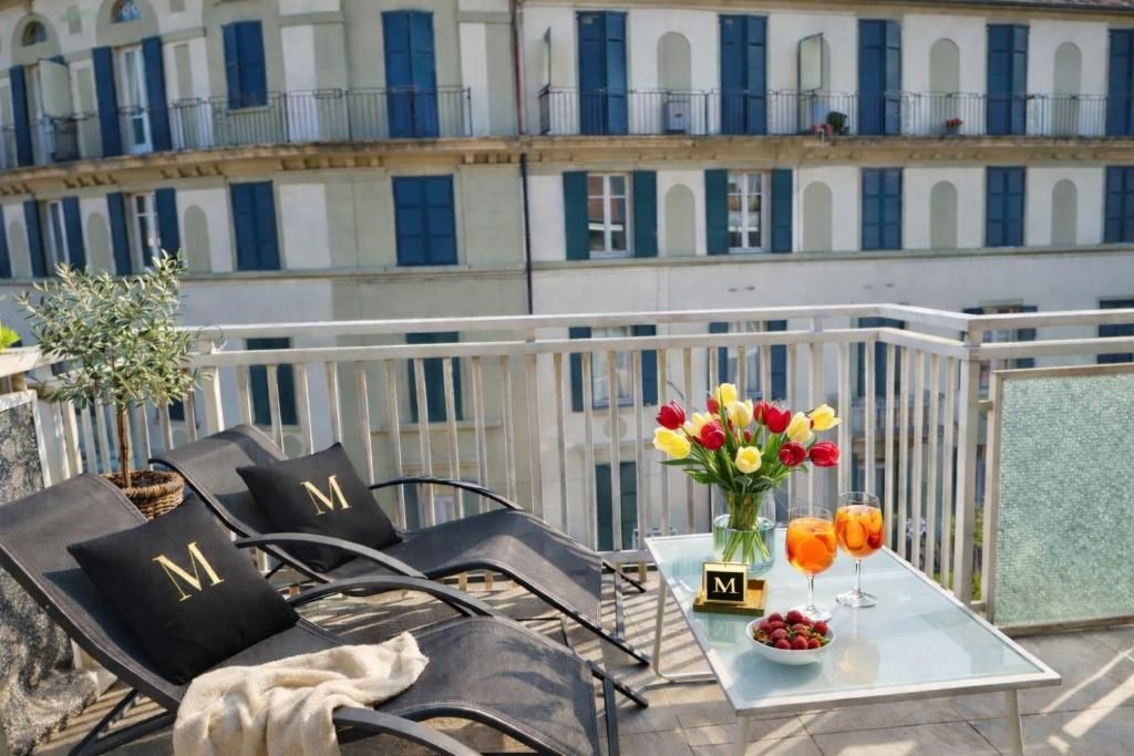 Ein Balkon mit zwei Liegestühlen, einem Tisch mit Blumenvase und einem Glas Orangensaft.