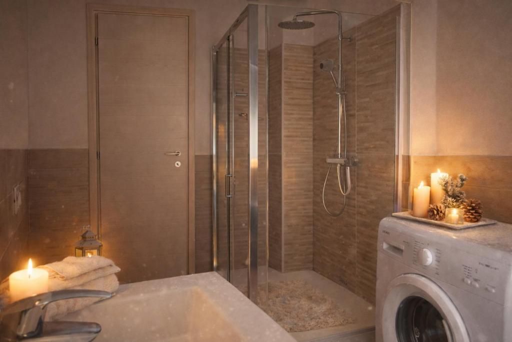A bathroom with a glass-enclosed shower, a washing machine, and a lit candle on the vanity.