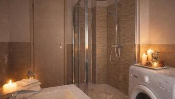 A bathroom with a glass-enclosed shower, a washing machine, and a lit candle on the vanity.