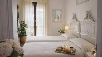 Habitación de hotel con dos camas, una mesita de noche con lámpara, ventana con cortinas y una bandeja con artículos de desayuno.