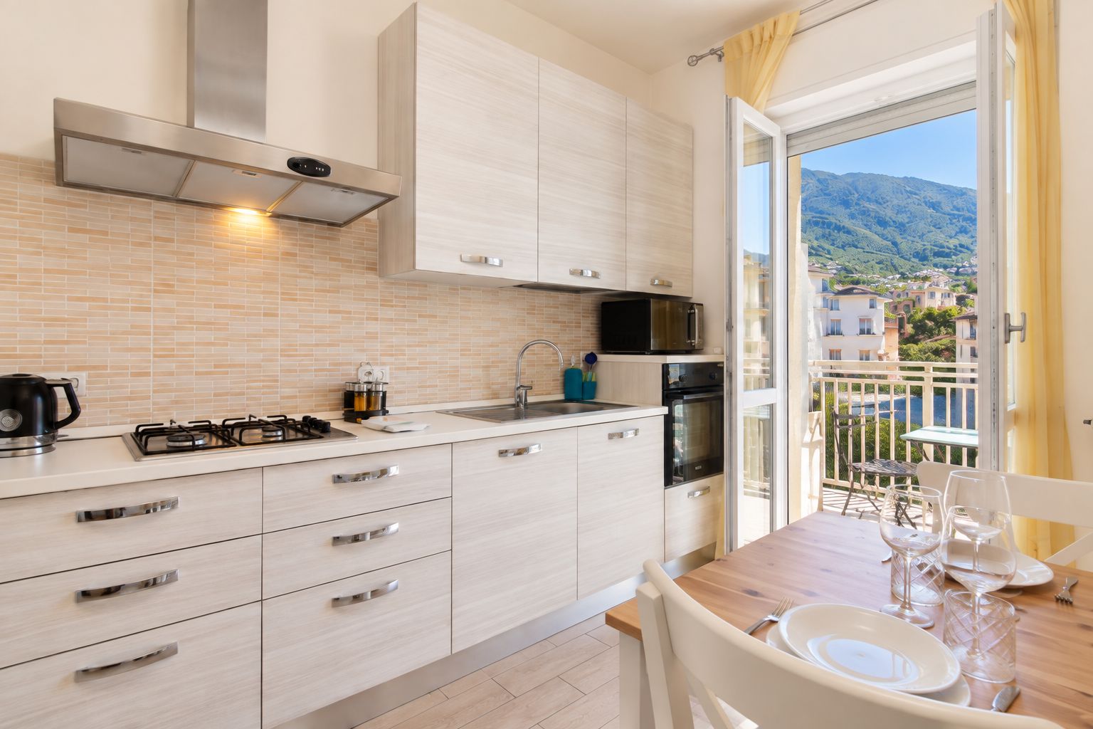Une cuisine moderne équipée d’une cuisinière à gaz, d’un four à micro-ondes et d’un four traditionnel, d’un évier et d’un coin repas avec une table dressée pour deux personnes.
