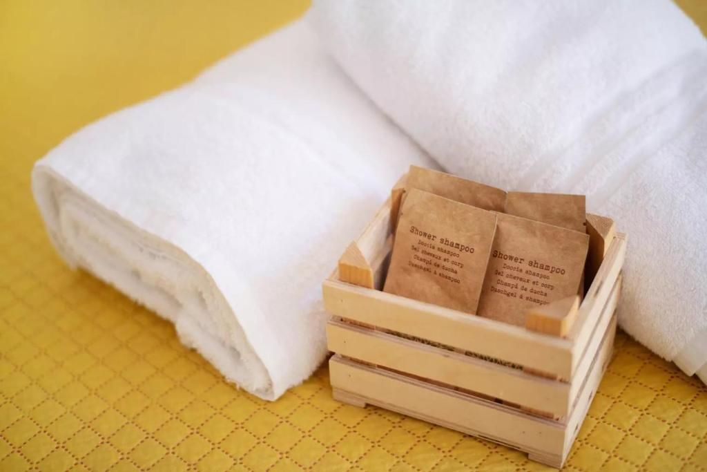 A stack of white towels and a wooden crate with two brown paper bags labeled 'Shower shampoo'.