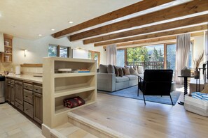 A spacious living area with a sofa, a black chair, and a wooden bookshelf. - Village Center 3G | Renovated 2BR in the Heart of Vail Village (Vail)