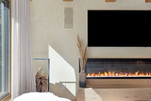 A modern living room with a fireplace, a flat-screen TV mounted above it, and a window with curtains. - Village Center 3G | Renovated 2BR in the Heart of Vail Village (Vail)