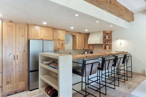 Une cuisine moderne avec des meubles en bois, un réfrigérateur en acier inoxydable et un coin bar équipé de tabourets.