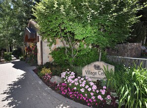 A sign for Village Center Condominiums surrounded by lush greenery and flowering plants. - Village Center 3G | Renovated 2BR in the Heart of Vail Village (Vail)