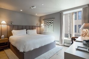 A modern hotel room with a large bed, bedside lamps, a window with curtains, and a desk with a lamp. - Village Center 3G | Renovated 2BR in the Heart of Vail Village (Vail)