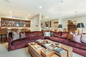 A spacious living room with a large sectional sofa, a coffee table, and a dining area with a wooden table and chairs. - Gore Place | 5BR Luxury Vail Home, Hot Tub & Ski Slope Views (Vail)