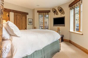 Un dormitorio con una cama grande, un televisor montado en la pared y un ventanal con vistas al exterior.