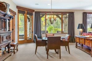 A dining area with a table and chairs, a chandelier, and a view through large windows. - Gore Place | 5BR Luxury Vail Home, Hot Tub & Ski Slope Views (Vail)