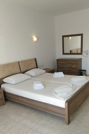 Hotellihuone, jossa on puinen sänky, yöpöytä, lipasto, peili ja seinään kiinnitetty valaisin.