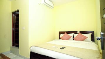 A single bed with a wooden headboard, two pillows, a remote control, and a small table with a basket.