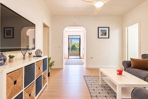 A modern living room with a sofa, a coffee table, and a TV. There is a hallway leading to a balcony with a view of greenery. - Villa Milano – 4 bedroom house with private pool & garden in Lubrin (La Rambla Aljibe)