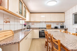 A kitchen with granite countertops, wooden cabinets, a built-in oven, and a dining area with wooden chairs. - Villa Milano – 4 bedroom house with private pool & garden in Lubrin (La Rambla Aljibe)