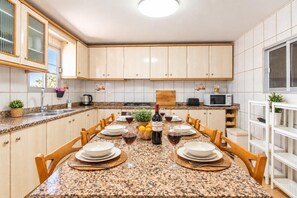 A kitchen with a granite countertop, wooden cabinets, and a dining table set for four with plates, glasses, and a bottle of wine. - Villa Milano – 4 bedroom house with private pool & garden in Lubrin (La Rambla Aljibe)