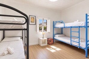 A dormitory room with bunk beds, a small bedside table with a lamp, a framed picture on the wall, and a window with a view. - Villa Milano – 4 bedroom house with private pool & garden in Lubrin (La Rambla Aljibe)