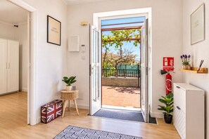 Un ingresso che dà su uno spazio esterno, con un estintore, un tavolino con una pianta e un quadro appeso al muro.