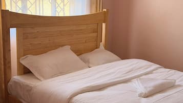 Un lit simple avec une tête de lit en bois, dans une pièce aux murs de couleur claire.