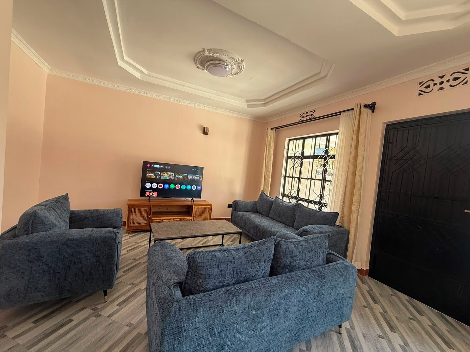 A living room with a flat-screen TV, two sofas, a coffee table, and a large window with curtains.