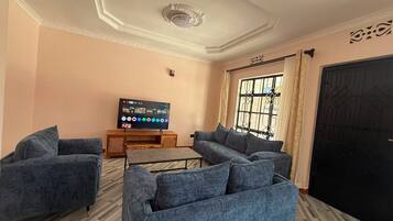 A living room with a flat-screen TV, two sofas, a coffee table, and a large window with curtains.