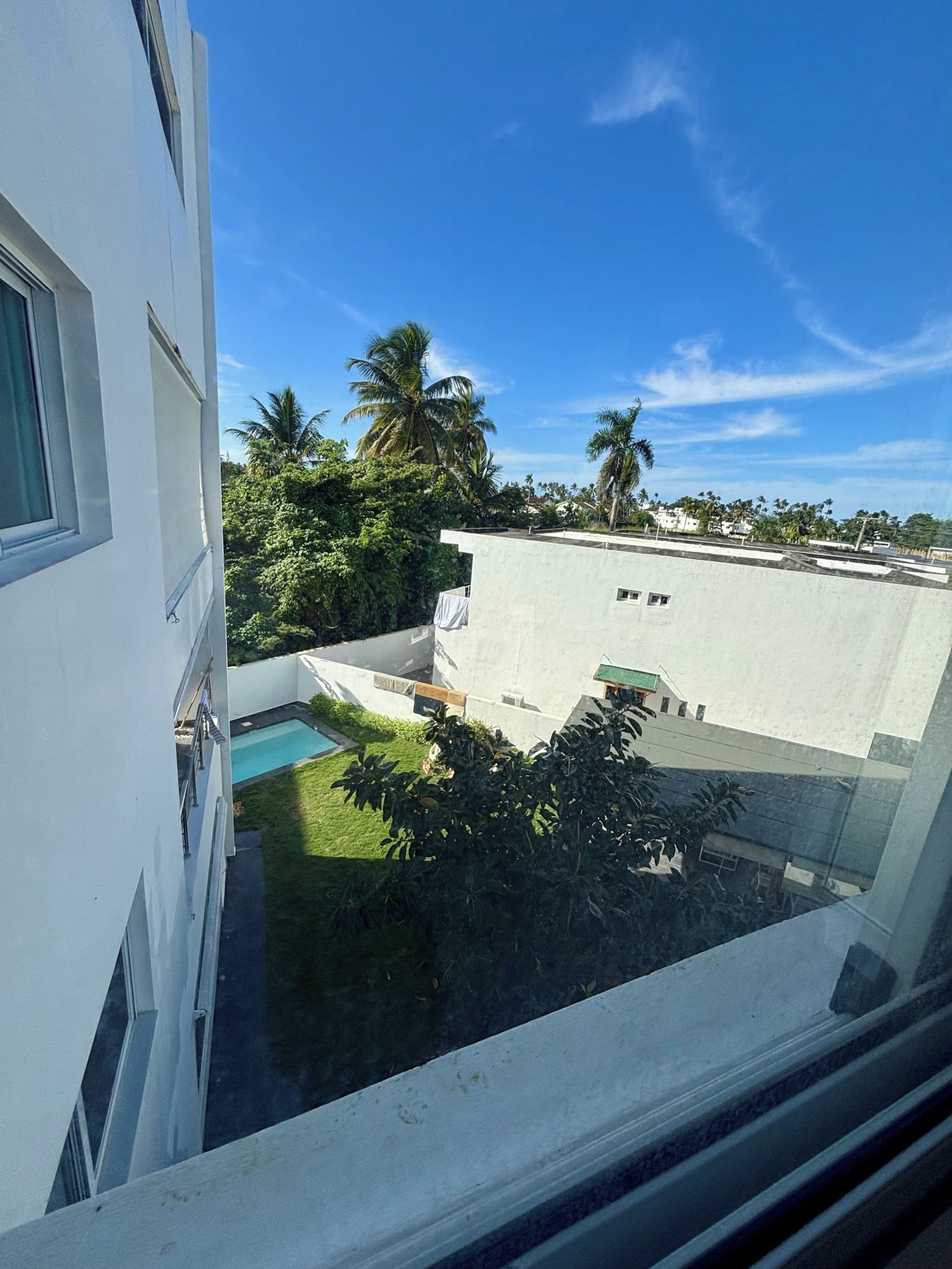 Un edificio residencial con piscina, rodeado de vegetación y palmeras.