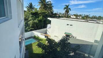 Un edificio residencial con piscina, rodeado de vegetación y palmeras.